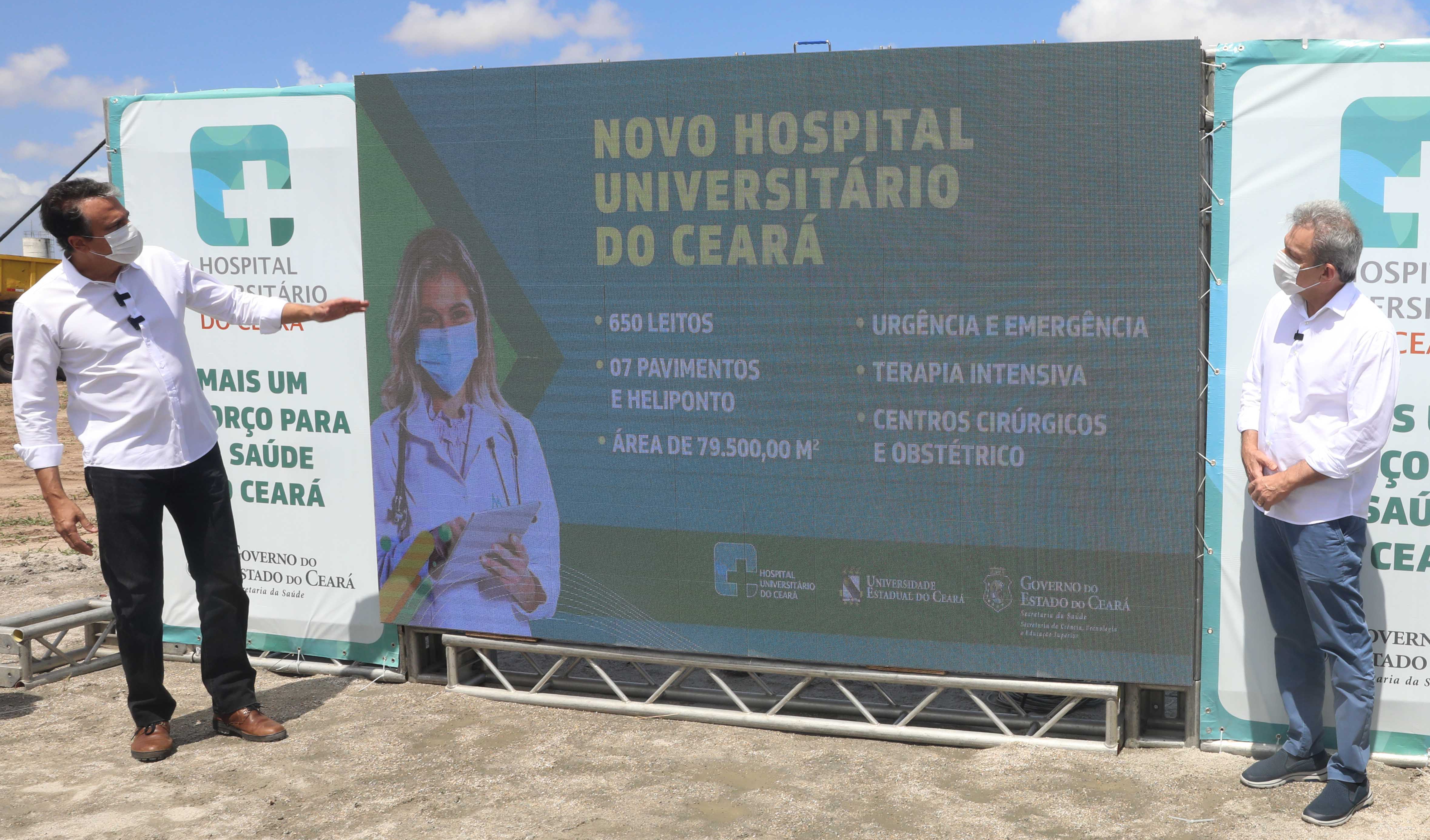 Governador apresentando projeto do hospital em telão e prefeito do outro lado do telão olhando